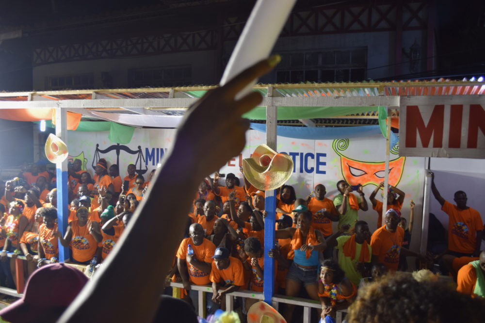 The parade route is lined with stands for different companies and government agencies. It’s a strange image: Roody is singing about state corruption and there is the ministry of justice dancing and singing along.